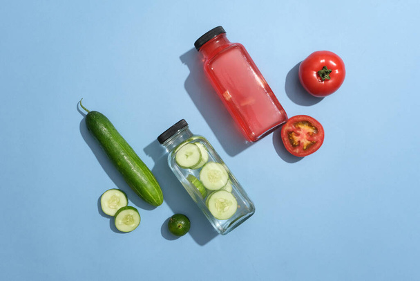 Widok z góry butelki szklane wypełnione wodą detox ogórka i soku pomidorowego wyświetlane na niebieskim tle. Projekt modelarski zdrowych marek napojów - Zdjęcie, obraz