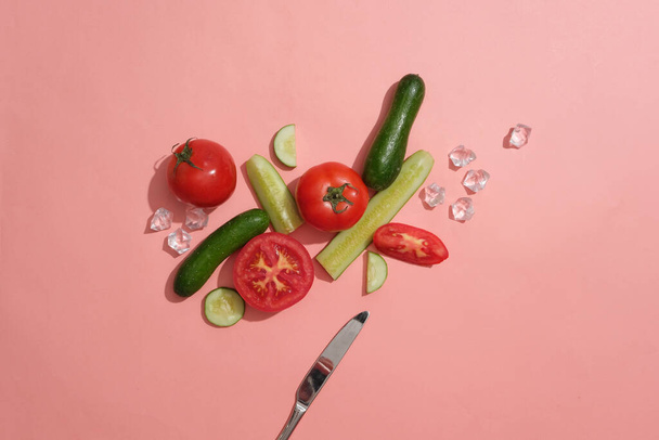Concombre et tomate coupés en tranches et moitiés décorées sur fond rose avec des glaçons et un couteau. Concept de fruits sains qui sont bons pour la peau et la santé - Photo, image