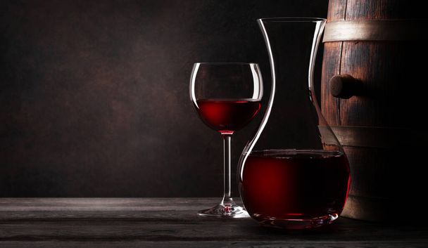 Wijn decanter, glas rode wijn en oude houten vat. met kopieerruimte - Foto, afbeelding
