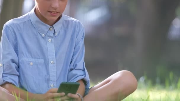 Gelukkige jonge tiener jongen praten op mobiele telefoon buiten in de zomer park. Online vriendschap concept. - Video
