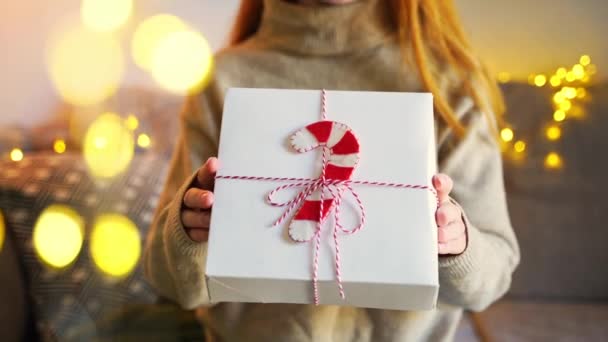 Close-up jonge vrouw in gezellige trui geeft een kerstpakket geschenkdoos. Opgewonden jong volwassene verpakt cadeau Nieuwjaarsdag viering en felicitatie - Video