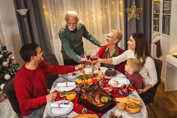Großvater prostet am Tisch zu. Familie feiert gemeinsam Weihnachten und isst hausgemachtes Essen. - Foto, Bild