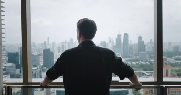 Widok z tyłu 30-letni biznesmen na wieżowcu patrzący na wielkie miasto marzący o ambicjach biznesowych i osiągnięciach. Milenijny biznesmen stojący na balkonie drapacza chmur. Koncepcja wielkich marzeń - Materiał filmowy, wideo