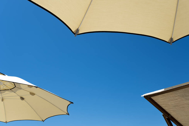 Minimum yaz tatili konsepti. Mavi gökyüzünün önündeki plaj şemsiyesi. Takılıyorum, plajda uzanıyorum.. - Fotoğraf, Görsel