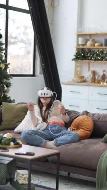V blízkosti vánočního stromečku sedí mladá a krásná žena a hraje videohry využívající sluchátka virtuální reality. Vysoce kvalitní 4K záběry - Záběry, video