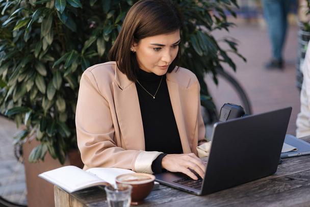 Attractive young female freelancer working on laptop on terrace in cafe. Woman photographer retouch photos on open air. High quality photo - Photo, Image