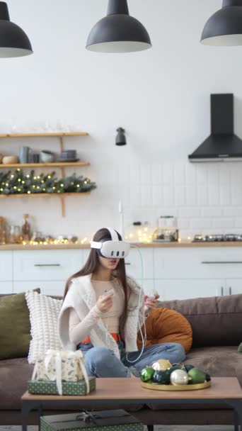 La giovane, bella signora siede vicino all'albero di Natale e gode di videogiochi attraverso un auricolare realtà virtuale. Filmati 4k di alta qualità - Filmati, video