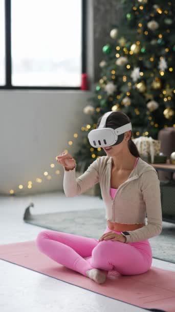 Девушка погружается в йогу дома во время праздников, используя гарнитуру виртуальной реальности. Высококачественные 4k кадры - Кадры, видео