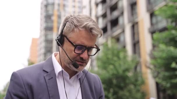 Бизнесмен в очках разговаривает онлайн, печатая на ноутбуке, сидя на улице. Бизнес, концепция технологий. Концепция реального времени - Кадры, видео