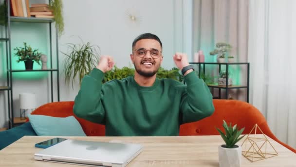 Boldog indiai férfi kiabál, ünnepli siker, győzelem, cél elérése jó hír lottó szerencse győzelem, nézi TV bajnokság a modern lakás. Arab srác az irodai szobában ül az asztalnál - Felvétel, videó