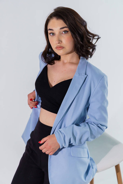 Beautiful young girl in black trousers and a blue jacket on a white background. Portrait of a young woman - Foto, afbeelding