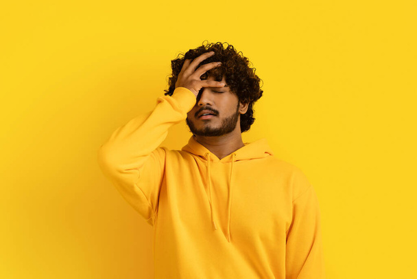 Hand, face and regret with black man in studio on yellow background feeling disappointed by a mistake. Facepalm, problem and frustrated with indian guy covering his eye while annoyed, upset or ashamed - 写真・画像