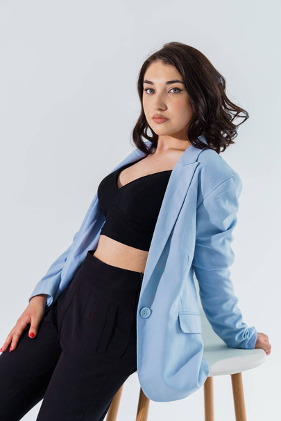 Beautiful young girl in black trousers and a blue jacket on a white background. Portrait of a young woman - Photo, Image