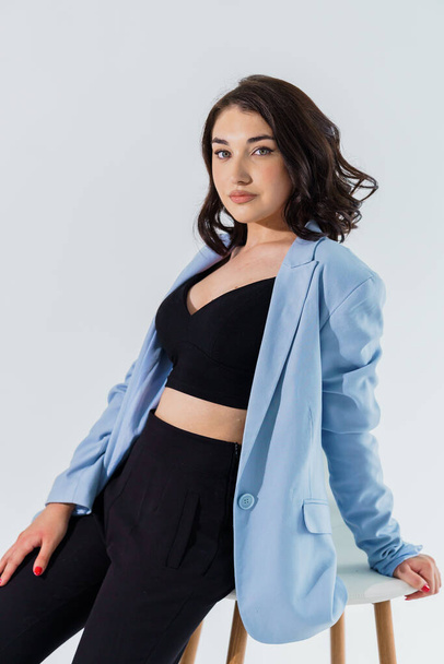 Siyah pantolonlu ve beyaz arka planda mavi ceketli güzel bir genç kız. Genç bir kadının portresi - Fotoğraf, Görsel