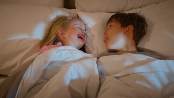 Zabawny biały starszy brat zrobić młodsza siostra śmiech show język grymaszenie w łóżku przed snem szczęśliwy śmiech dzieci chłopiec dziewczyna bawiąc się razem o zabawy rodzeństwo uczucie związek - Materiał filmowy, wideo