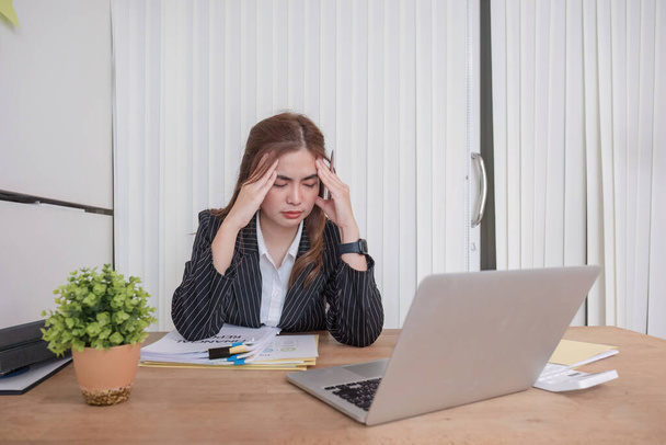 Азіатська бізнес-леді втомилася і стресує під час роботи з фокусом на ноутбуці в сучасному офісі. - Фото, зображення
