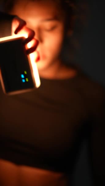 Em um salão mal iluminado, uma jovem senhora em roupas escuras dança energeticamente, segurando uma luz. Imagens 4k de alta qualidade - Filmagem, Vídeo