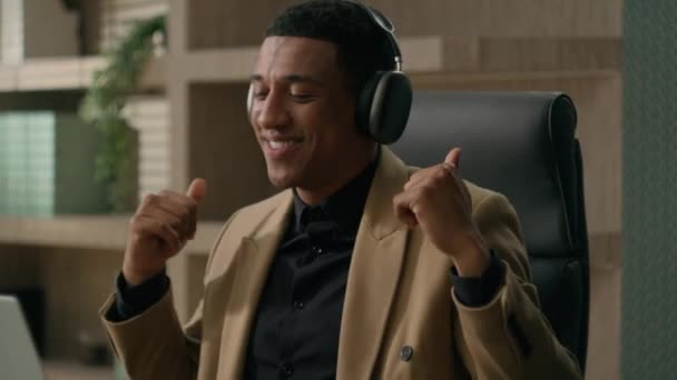 Carefree radostný Afroameričan šťastný obchodník poslouchat hudbu ve sluchátkách relaxovat na pracovišti tanec podnikatel poslech píseň ve sluchátkách legrační směšný tanec on-line audio služby na notebooku - Záběry, video