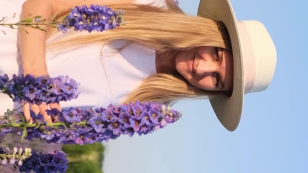 花畑で帽子を被った若い女性. バーティカルビデオ. - 映像、動画