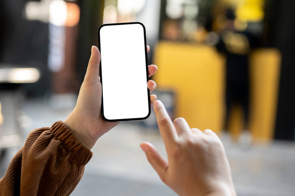 Detailní záběr na maketu chytrého telefonu s bílou obrazovkou v ruce ženy s rozmazaným pozadím maloobchodu na ulici. mobilní bankovnictví, pomocí mapy na telefonu, textové zprávy - Fotografie, Obrázek