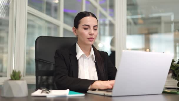 Koncentrált női irodai dolgozó ül az asztalnál, és gépel a vezeték nélküli laptop billentyűzeten, miközben hátfájást érez. Kaukázusi beteg hölgy próbál nyúlik vissza a munkahelyen tágas szobában. - Felvétel, videó