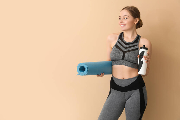 Sportliche junge Frau mit Yogamatte und Wasserflasche auf beigem Hintergrund - Foto, Bild