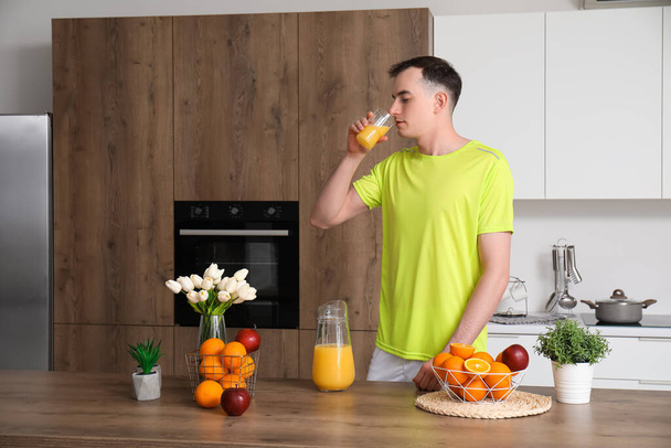 若いです男飲むオレンジジュースでキッチン - 写真・画像