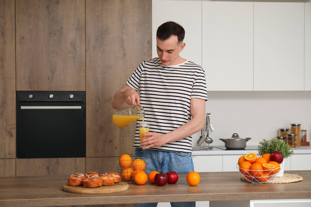 Nuori mies kaataa appelsiinimehua lasiin keittiössä - Valokuva, kuva