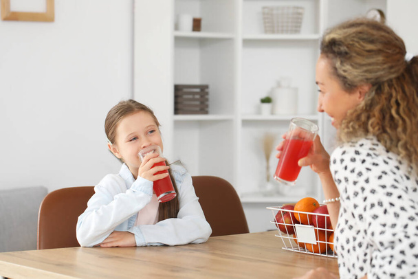 Bambina con sua madre che beve succo di frutta in cucina - Foto, immagini