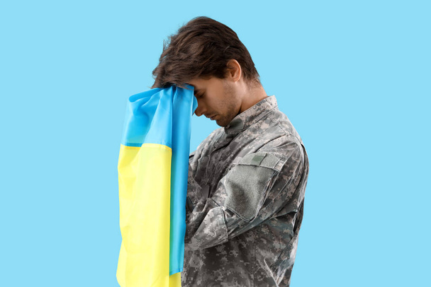 青い背景で祈るウクライナの旗を持つ若い男性兵士 - 写真・画像