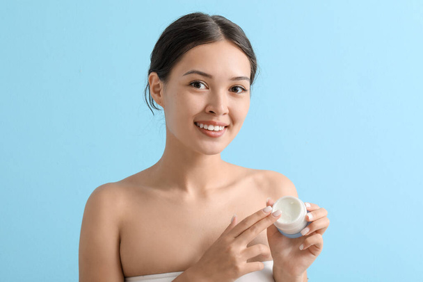 Beautiful Asian woman with jar of cream on blue background, closeup - Photo, Image
