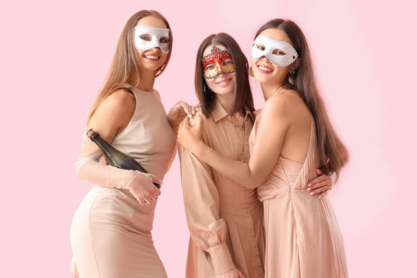 Kauniita nuoria naisia karnevaali naamiot pullo samppanjaa vaaleanpunainen tausta - Valokuva, kuva