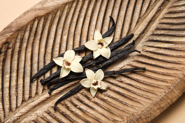Dřevěné desky s aromatickými vanilkovými tyčinkami a květy na béžovém pozadí - Fotografie, Obrázek