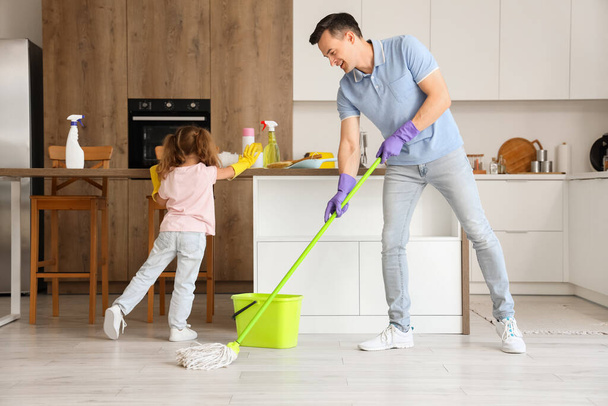 Χαριτωμένο κοριτσάκι με τον μπαμπά της να καθαρίζει στην κουζίνα. - Φωτογραφία, εικόνα