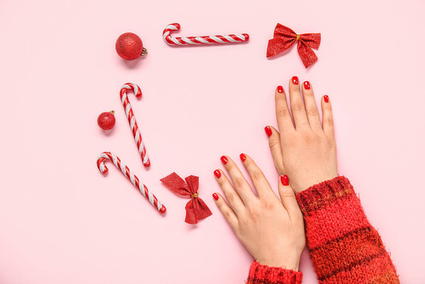 Руки женщины с красным маникюром и рождественским декором на розовом фоне - Фото, изображение