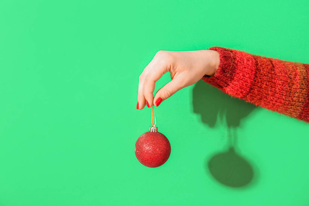 Жіноча рука з червоним манікюром, що тримає різдвяний м'яч на зеленому фоні - Фото, зображення