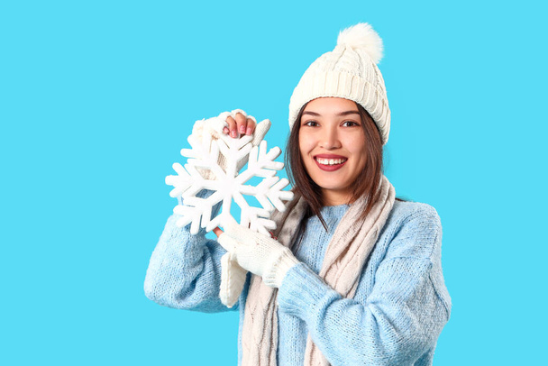Young Asian woman in winter clothes with snowflake on blue background - Photo, Image