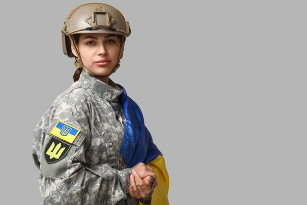 Молодая женщина-солдат в форме с флагом Украины на сером фоне - Фото, изображение