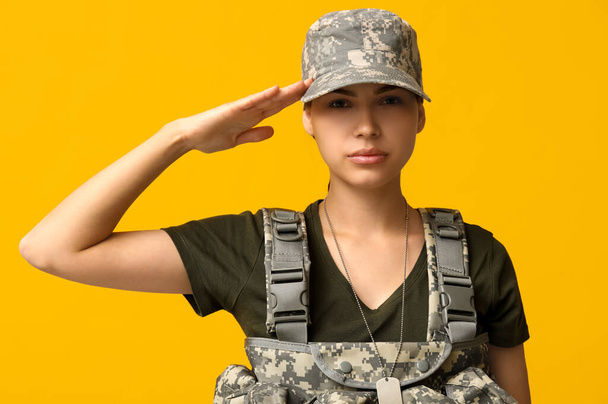 Αυτοπεποίθηση νεαρή γυναίκα στρατιώτης με στολή χαιρετισμό σε κίτρινο φόντο - Φωτογραφία, εικόνα