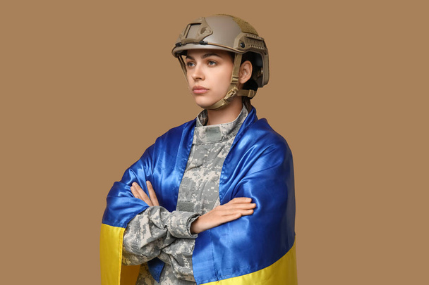 Jeune soldat femme en uniforme avec drapeau de l'Ukraine sur fond beige - Photo, image