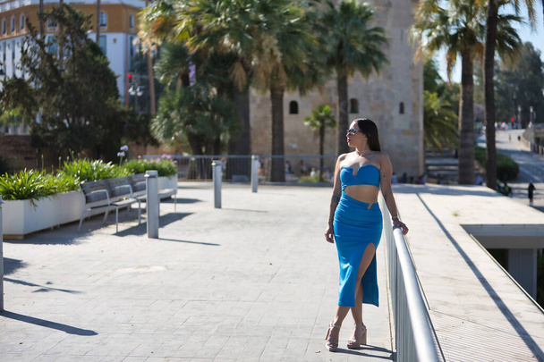 Junge, schöne, brünette, südamerikanische Frau in blauem Kleid und Sonnenbrille auf Reisen in einer europäischen Stadt. Konzept Schönheit, Mode, Trend, Reisen, Urlaub. - Foto, Bild