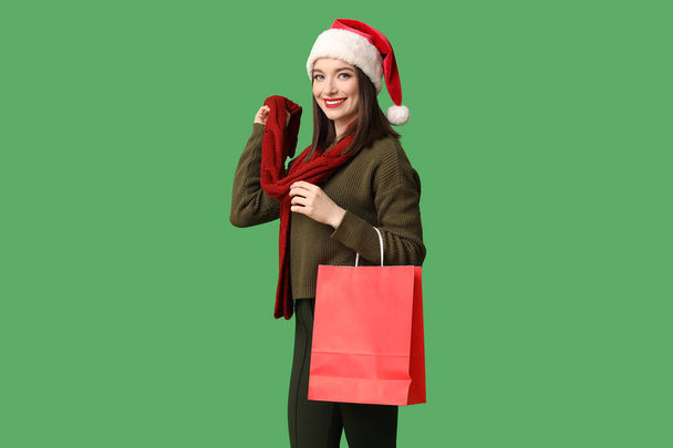 Young woman in Santa hat with shopping bag on green background - Photo, Image