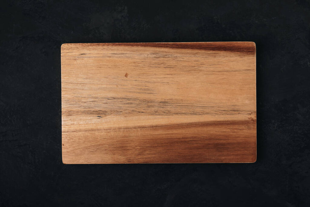 Tabla de cortar de madera sobre fondo de hormigón de piedra oscura, vista superior - Foto, Imagen