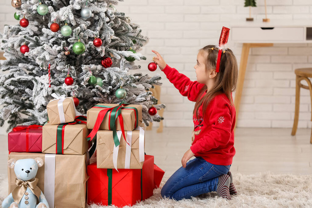 Roztomilé holčička v Santa klobouk čelenka zdobení vánoční stromeček a dárkové krabice doma - Fotografie, Obrázek