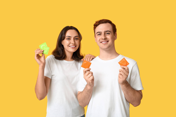 Jong stel met condooms op gele achtergrond. Veilig seksconcept - Foto, afbeelding