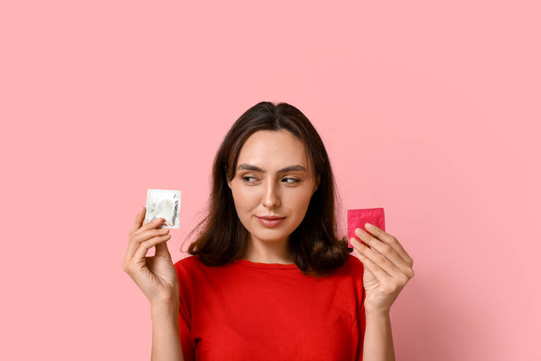 Mujer joven con condones sobre fondo rosa. Concepto de sexo seguro - Foto, imagen