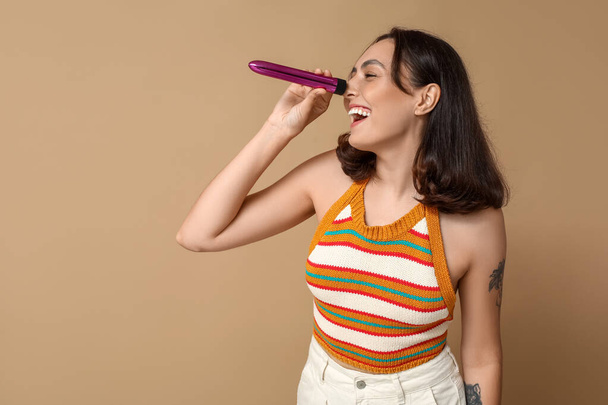 Funny young woman with vibrator on beige background - Photo, Image
