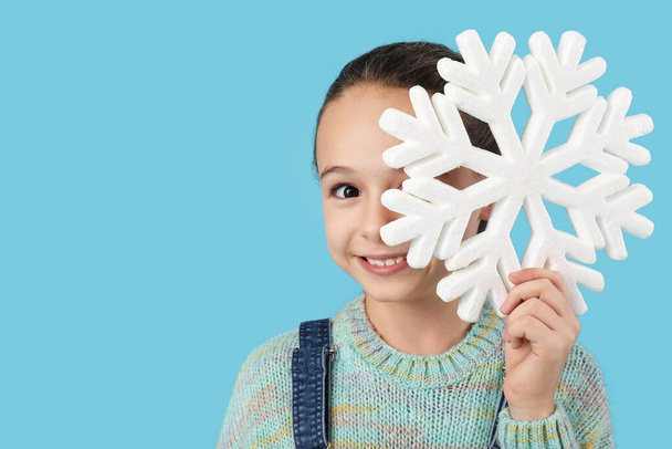 Милая маленькая девочка с декоративной снежинкой на синем фоне - Фото, изображение