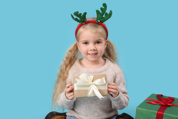 Милая маленькая девочка с оленьими рогами и подарками на синем фоне - Фото, изображение