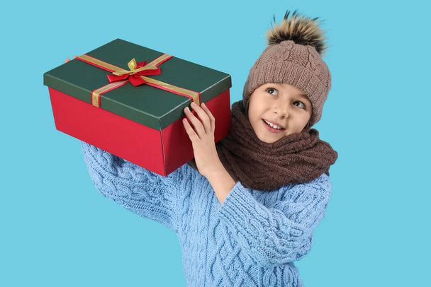 Cute little girl in winter clothes with gift box on blue background - Photo, Image